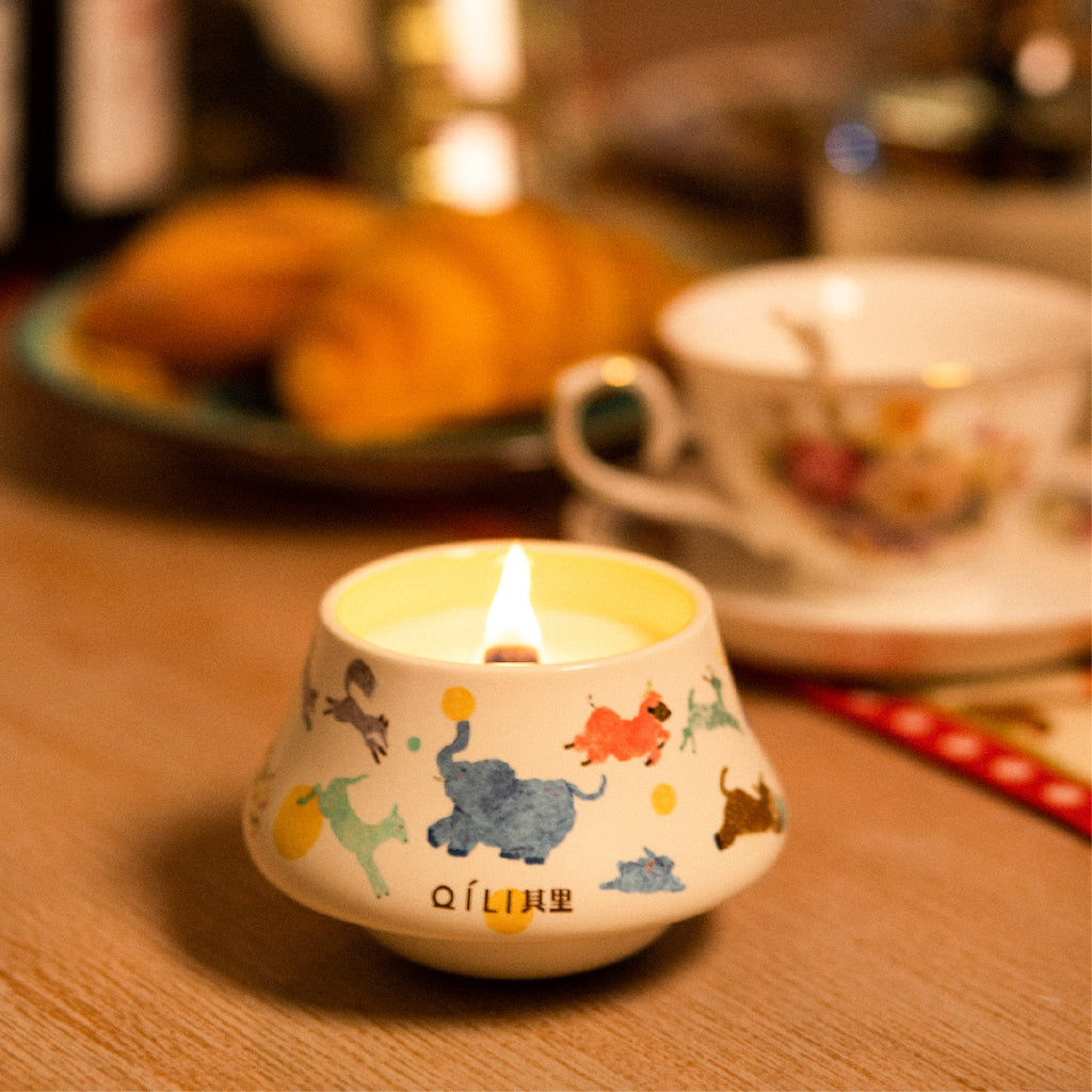 Scented candle in illustrated ceramic cup with visible flame on wood