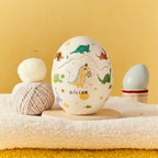 Dinosaur egg scented candle with pastel dino print on white egg-shaped container