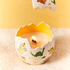 Dinosaur egg scented candle with lit flame inside molded opening, dino print