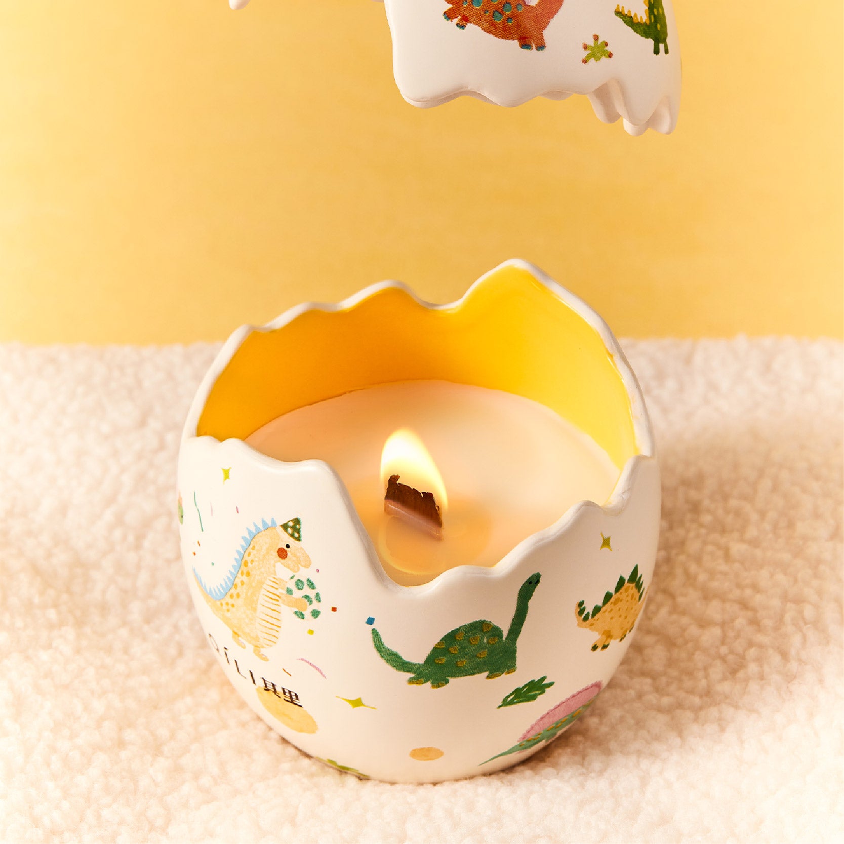 Dinosaur egg scented candle with lit flame inside molded opening, dino print